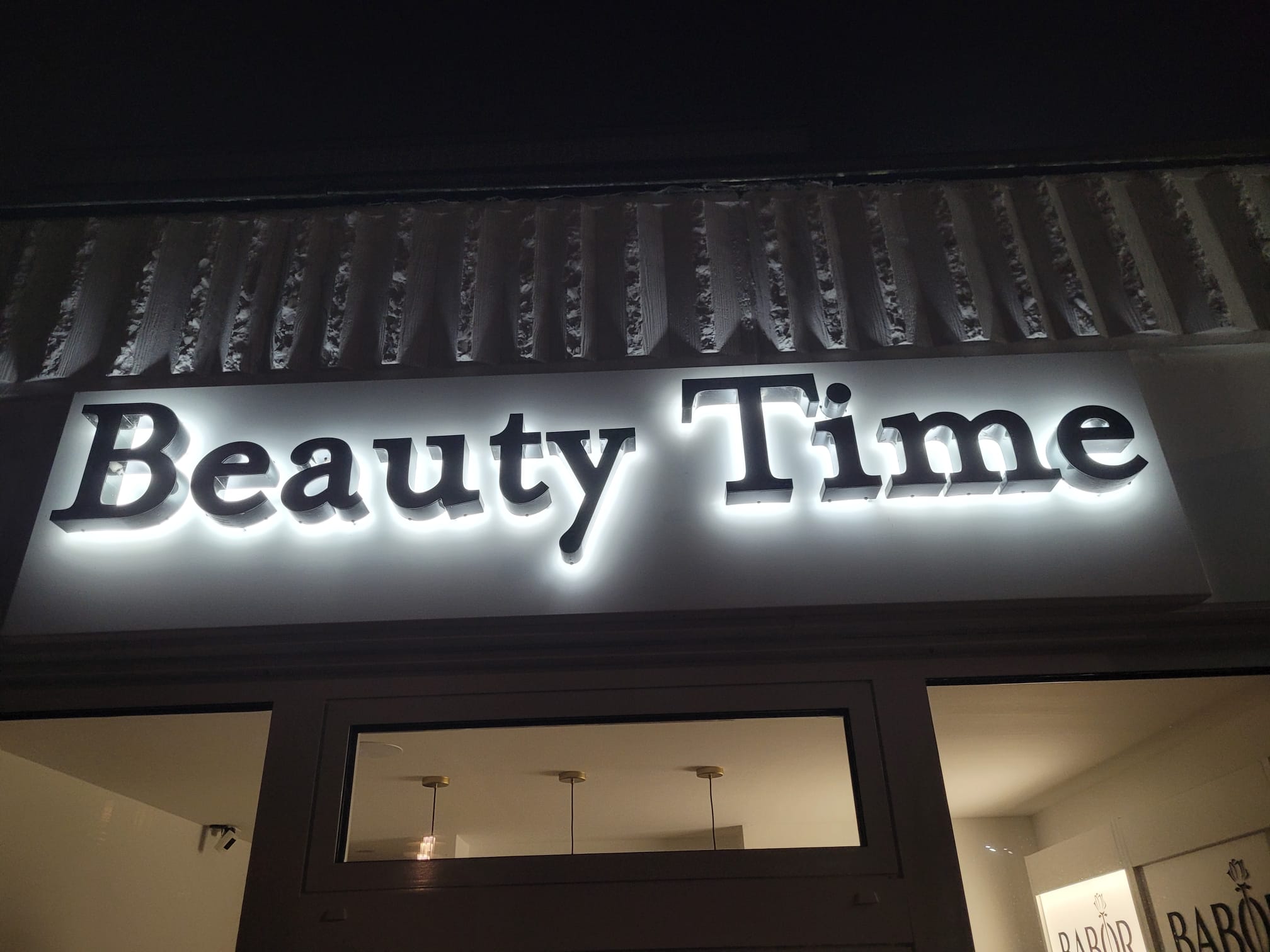 Leuchtender Beauty-Time-Schriftzug über dem Schaufenster bei Nacht