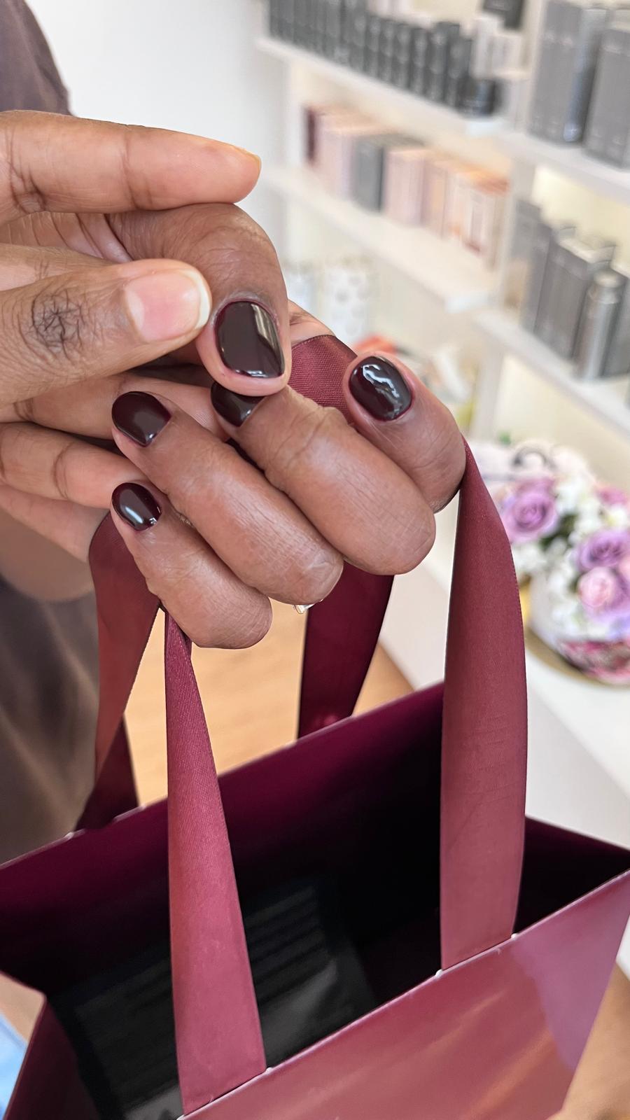 Maniküre mit dunkelbraunem Nagellack, die Hand hält eine Geschenktüte