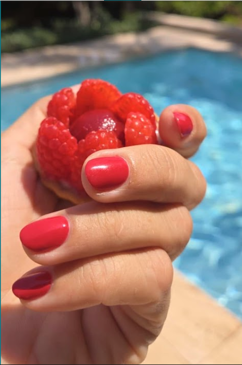 Roter Nagellack, die Hand hält Himbeeren am Pool